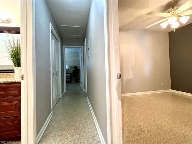 Hall with attic access, baseboards, and dark aggregate flooring