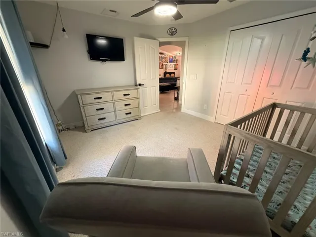 Bedroom featuring a crib, light carpet, and a ceiling fan