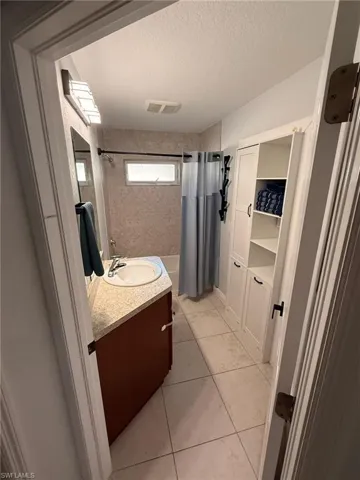 Bathroom with vanity, a textured ceiling, shower / bath combo with shower curtain, and light tile patterned flooring
