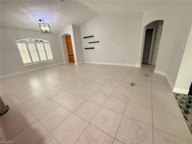 Spare room with arched walkways, lofted ceiling, light tile patterned floors, and a chandelier