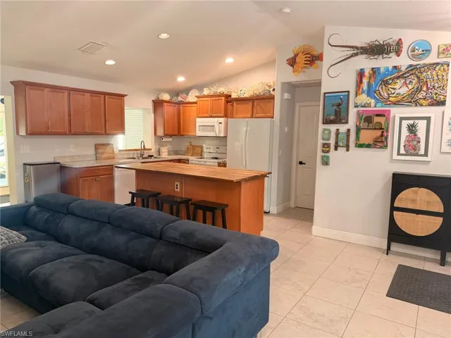 Kitchen featuring a kitchen island, wood finish cabinets, wooden counters, white appliances, and a kitchen breakfast bar