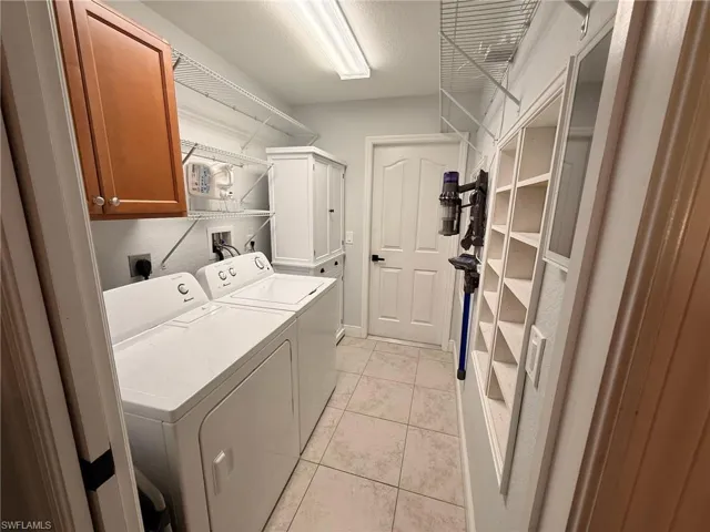 Laundry area featuring cabinet space, light tile patterned flooring, washing machine and dryer, and a textured ceiling