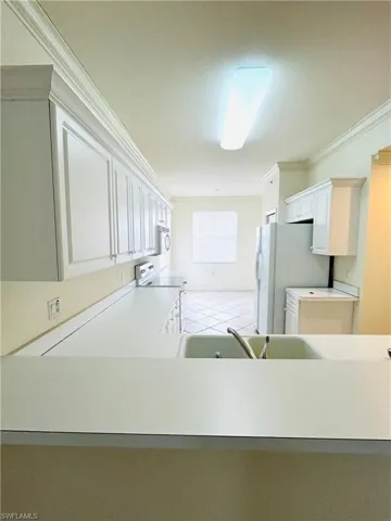 Kitchen featuring white cabinetry with crown molding, white countertops, a double basin sink with chrome faucet, and white appliances