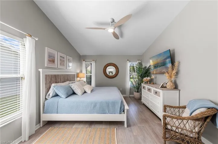 Vaulted ceiling bedroom featuring wood-finish flooring, two window openings with blinds, and a contemporary ceiling fan