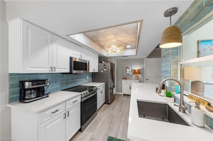 Modern kitchen featuring white cabinetry, a teal subway tile backsplash, stainless steel appliances, white countertops, and wood-finish flooring