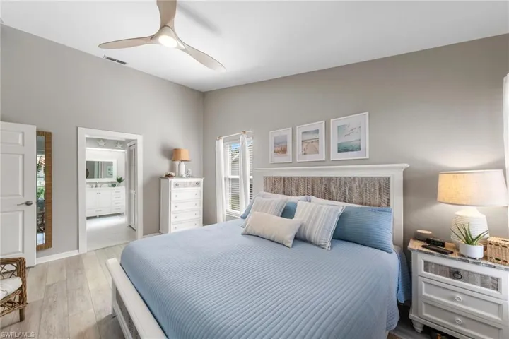 Spacious bedroom with light wood-finish flooring, a contemporary ceiling fan, and an en-suite bathroom featuring a dual vanity and mirror