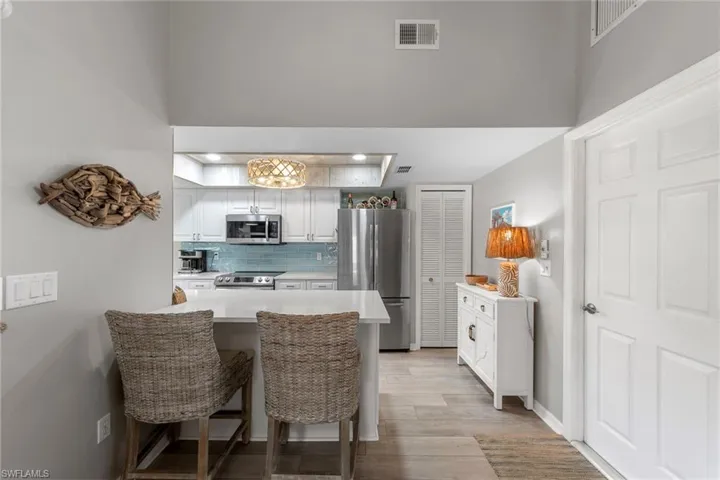 Open kitchen featuring a breakfast bar with seating, stainless steel appliances, white cabinetry, and a light blue tile backsplash
