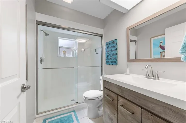 Bathroom featuring a glass-enclosed shower, a wood-finish vanity with an integrated sink, a large framed mirror, and a skylight