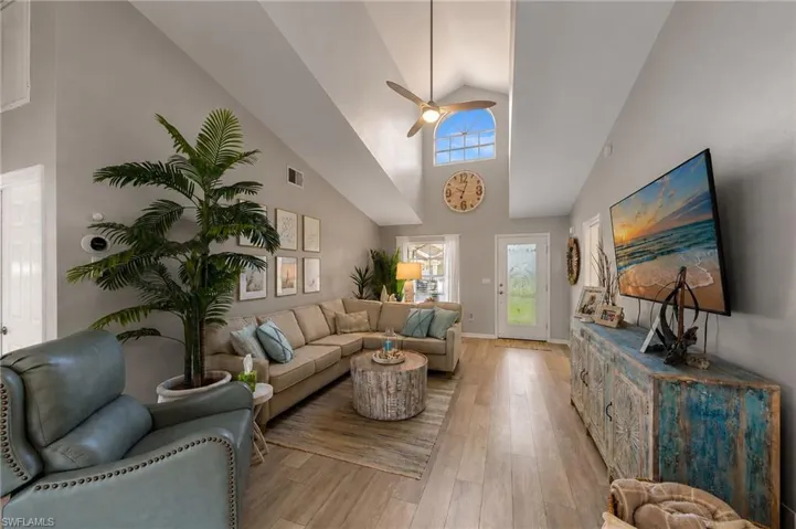 Vaulted ceiling living area featuring wood-finish flooring, an arched transom window, and a ceiling fan