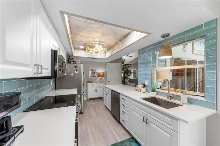 Bright kitchen featuring white cabinetry, light wood-finish flooring, a unique wood-paneled ceiling accent, and a light blue tile backsplash