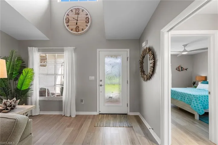 Entryway featuring wood-finish flooring, a white paneled door with frosted glass, and a large window with white blinds