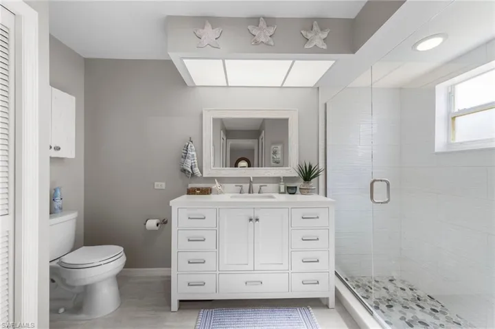 Bathroom featuring a white vanity with extensive drawer storage, a frameless glass shower enclosure, and a walk-in shower with pebble tile flooring