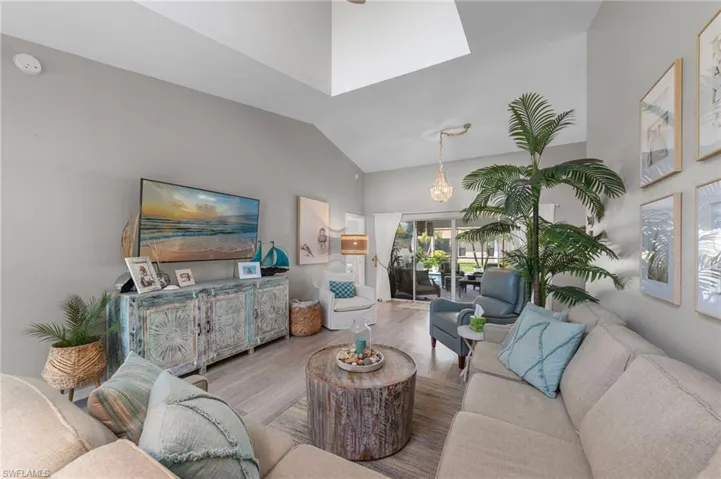 Spacious living area featuring light-toned wood-finish flooring, vaulted ceilings with skylight, and sliding glass doors providing access to an outdoor patio