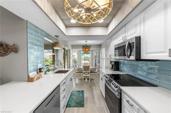 Galley kitchen featuring white cabinetry, light countertops, stainless steel appliances, a tile backsplash, and wood-finish flooring