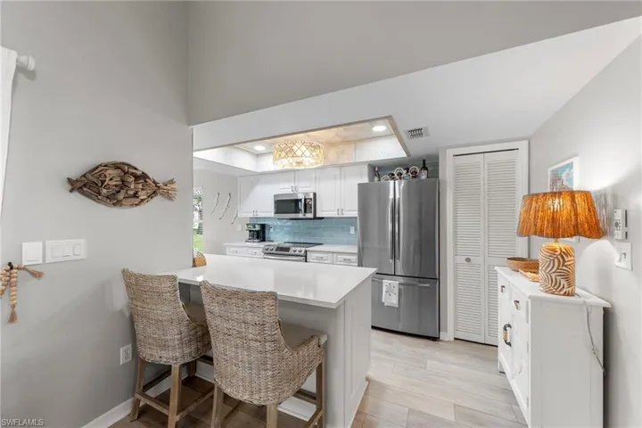 Modern kitchen featuring white cabinetry, stainless steel appliances, a white countertop island, a blue glass tile backsplash, and light wood-finish flooring