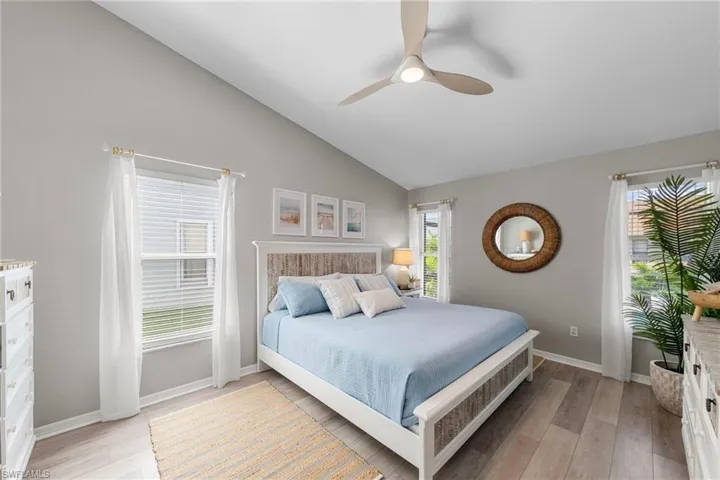 Vaulted ceiling bedroom featuring light wood-finish flooring, multiple windows, a ceiling fan with integrated lighting, and neutral wall tones