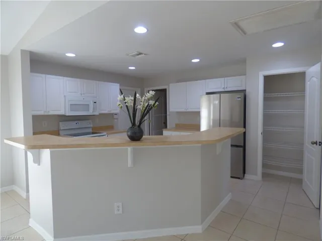 Kitchen featuring light countertops, white appliances, white cabinetry, a kitchen breakfast bar, and recessed lighting