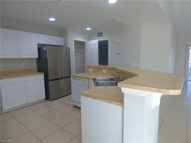 Kitchen featuring an island with sink and breakfast bar, white cabinets, light countertops, Pantry, Brand new side-by-side refrigerator, with French freezer door and recessed lighting.