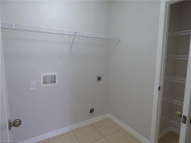 Laundry room featuring light tile floors, hookup for a washing machine, and hookup for an electric dryer with additional linen closet