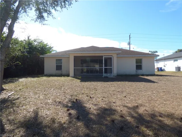 Rear view of house featuring stucco siding, a large backyard, and screened lanai