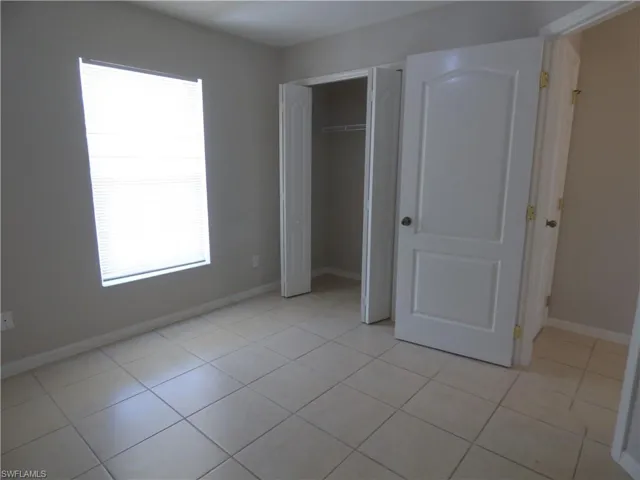 Guest bedroom with light tile patterned floors and a closet and window.