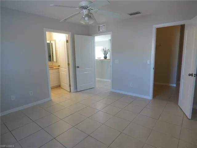 Master bedroom featuring light tile patterned floors, a spacious walk-in closet, and a ceiling fan. Entry to full bath and exit to kitchen area.