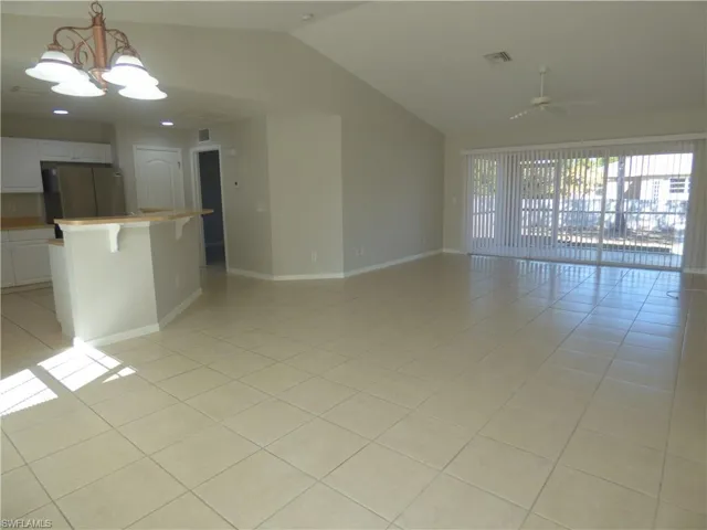 View from front entry to great room with a chandelier, light tile patterned floors, and vaulted ceiling.