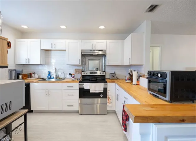 Kitchen featuring stainless steel electric range, white cabinetry, and wooden counters