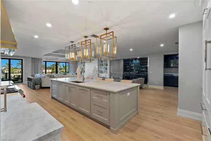 Kitchen with open floor plan, hanging light fixtures, a kitchen island with sink, light stone countertops, and gray cabinetry