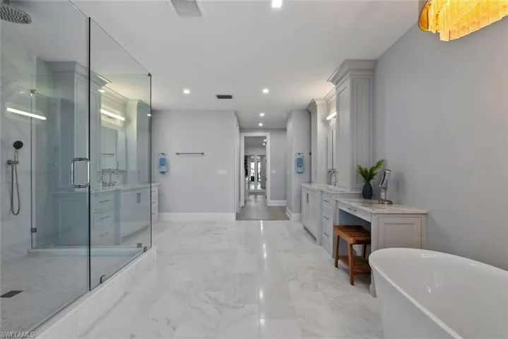 Master bath featuring two vanities, a marble finish shower, a freestanding tub, light marble finish floors, and recessed lighting