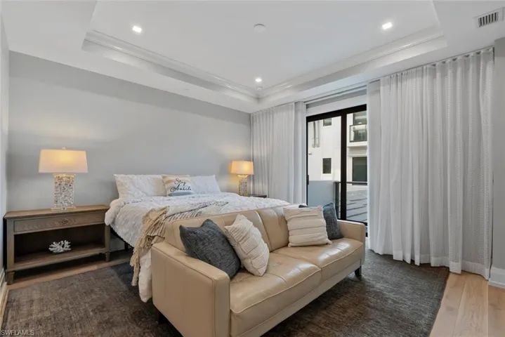 Bedroom featuring wood finished floors, a raised ceiling, recessed lighting, crown molding, and access to exterior