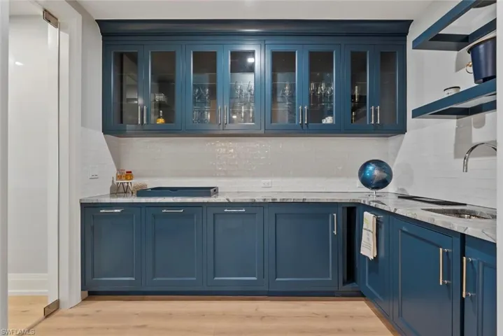 Bar  with blue cabinetry, light stone counters, open shelves, glass insert cabinets, and light wood-style floors