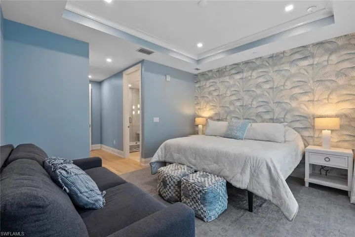 Bedroom featuring an accent wall, recessed lighting, a tray ceiling, light wood-type flooring, and ensuite bathroom