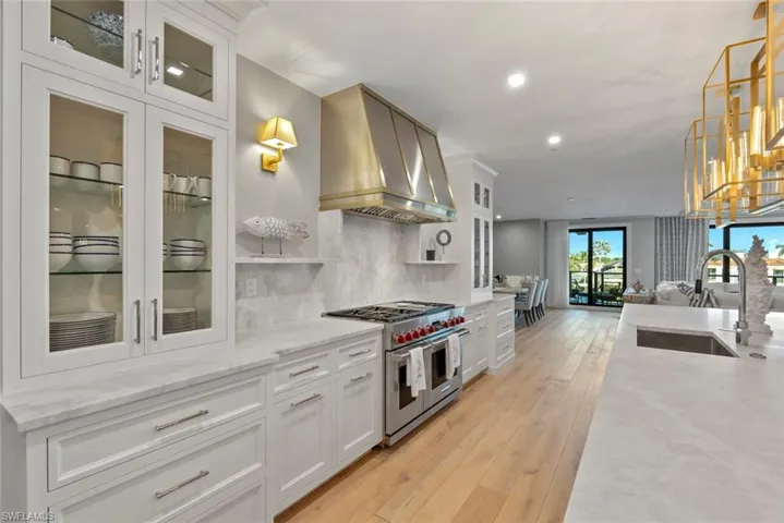 Kitchen with white cabinets, glass insert cabinets, tasteful backsplash, light stone countertops, and wall chimney range hood