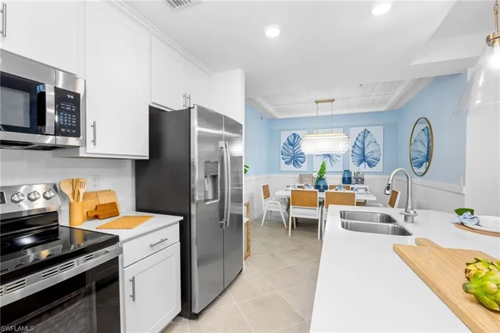 Kitchen with appliances with stainless steel finishes, light countertops, white cabinets, light tile patterned floors, and pendant lighting