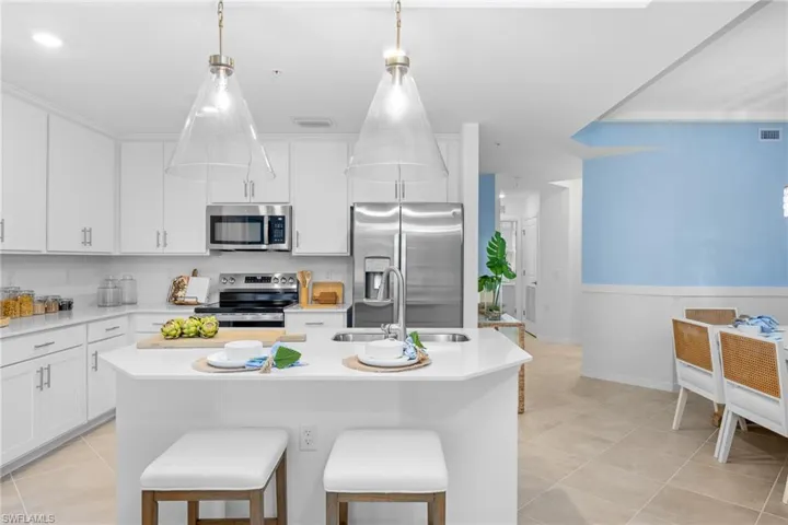 Kitchen featuring stainless steel appliances, light countertops, light tile patterned floors, white cabinetry, and an island with sink
