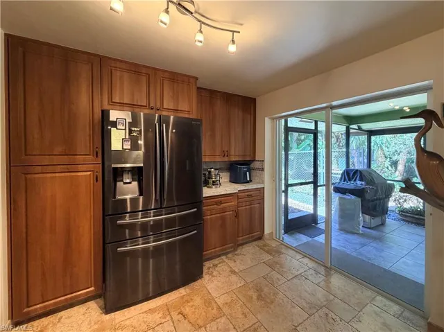 Kitchen with stainless steel refrigerator with ice dispenser, wood finish cabinets, stone countertops, and travertine tile floors