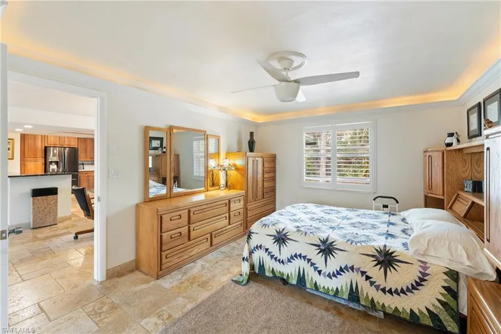 Bedroom with stone tile flooring, ceiling fan, ornamental molding, and stainless steel fridge