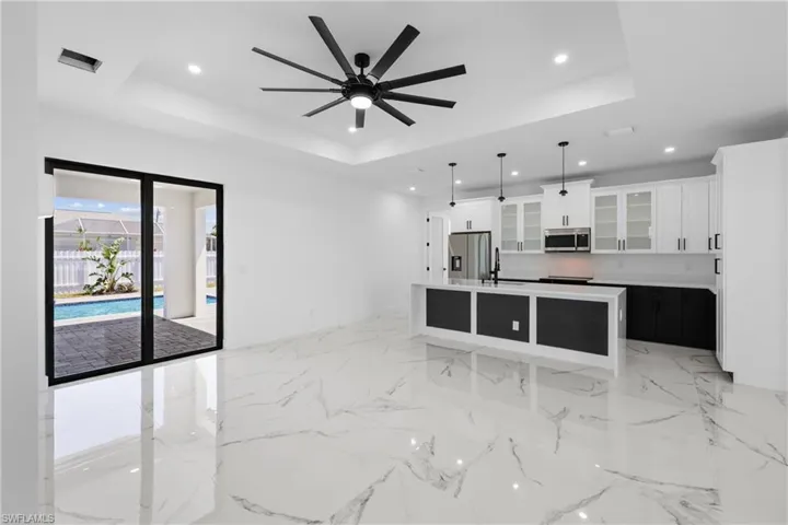 Kitchen featuring a sink, a ceiling fan, a raised ceiling, appliances with stainless steel finishes, and a large island