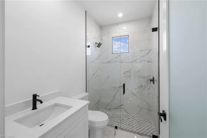 Full bathroom featuring toilet, vanity, a marble finish shower, marble finish floor, and recessed lighting