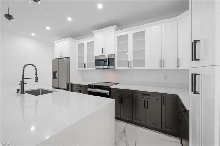 Kitchen with light stone counters, a sink, electric range oven, stainless steel microwave, and fridge with ice dispenser