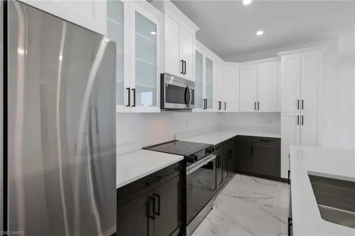Kitchen with marble finish floor, stainless steel appliances, recessed lighting, glass insert cabinets, and white cabinetry