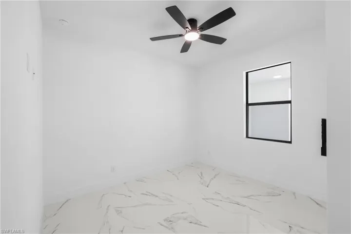 Empty room featuring marble finish floor, baseboards, and ceiling fan