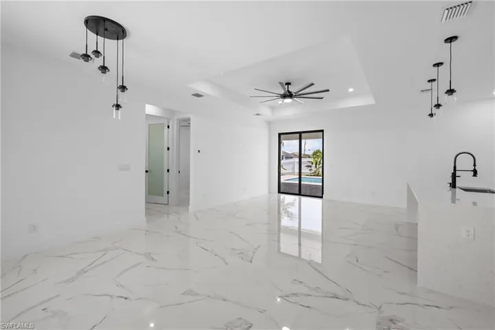Empty room with a tray ceiling, marble finish floor, visible vents, and ceiling fan