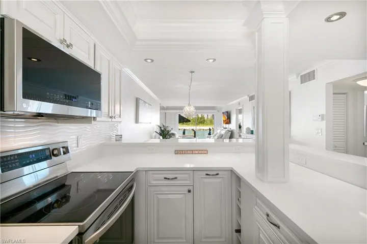 Kitchen with stainless steel appliances, white cabinetry, backsplash, decorative light fixtures, and light stone countertops