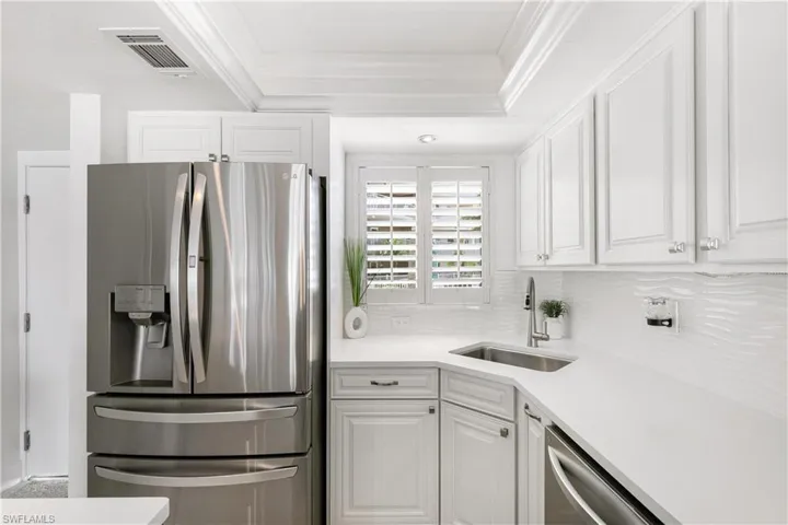 Kitchen with stainless steel appliances, white cabinetry, a raised ceiling, light stone counters, and decorative backsplash