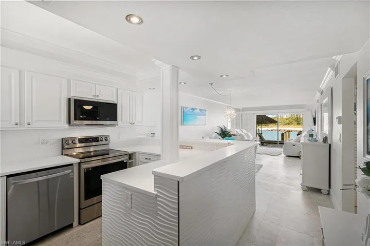 Kitchen featuring ornamental molding, stainless steel appliances, white cabinetry, open floor plan, and a chandelier