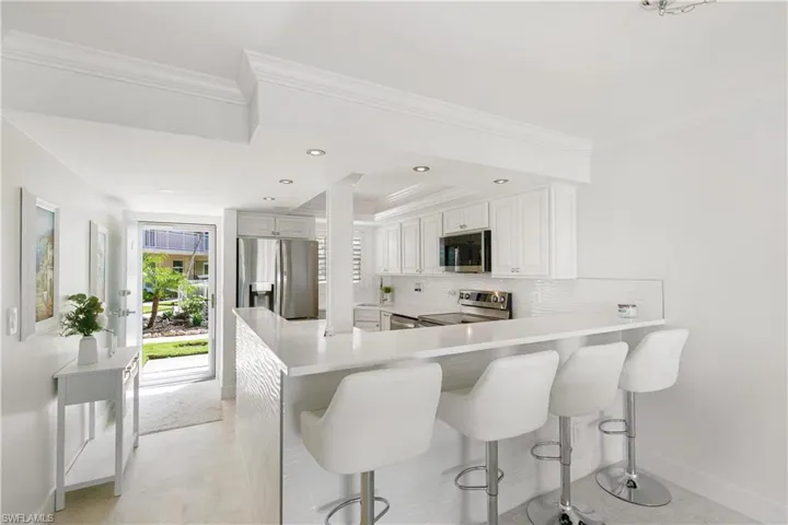Kitchen featuring a peninsula, stainless steel appliances, backsplash, white cabinetry, and a breakfast bar area