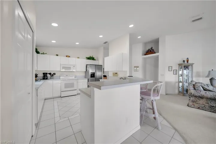 Kitchen with white cabinetry, a breakfast bar, light countertops, white appliances, and recessed lighting