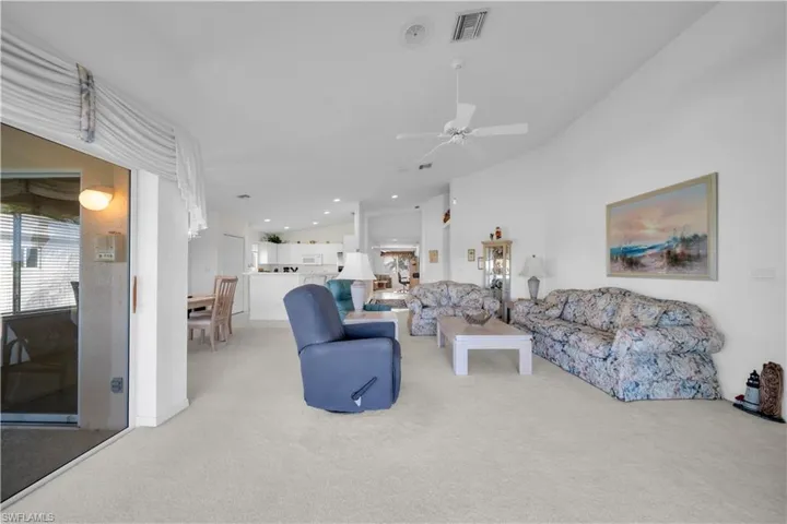 Living area featuring light colored carpet, lofted ceiling, and ceiling fan